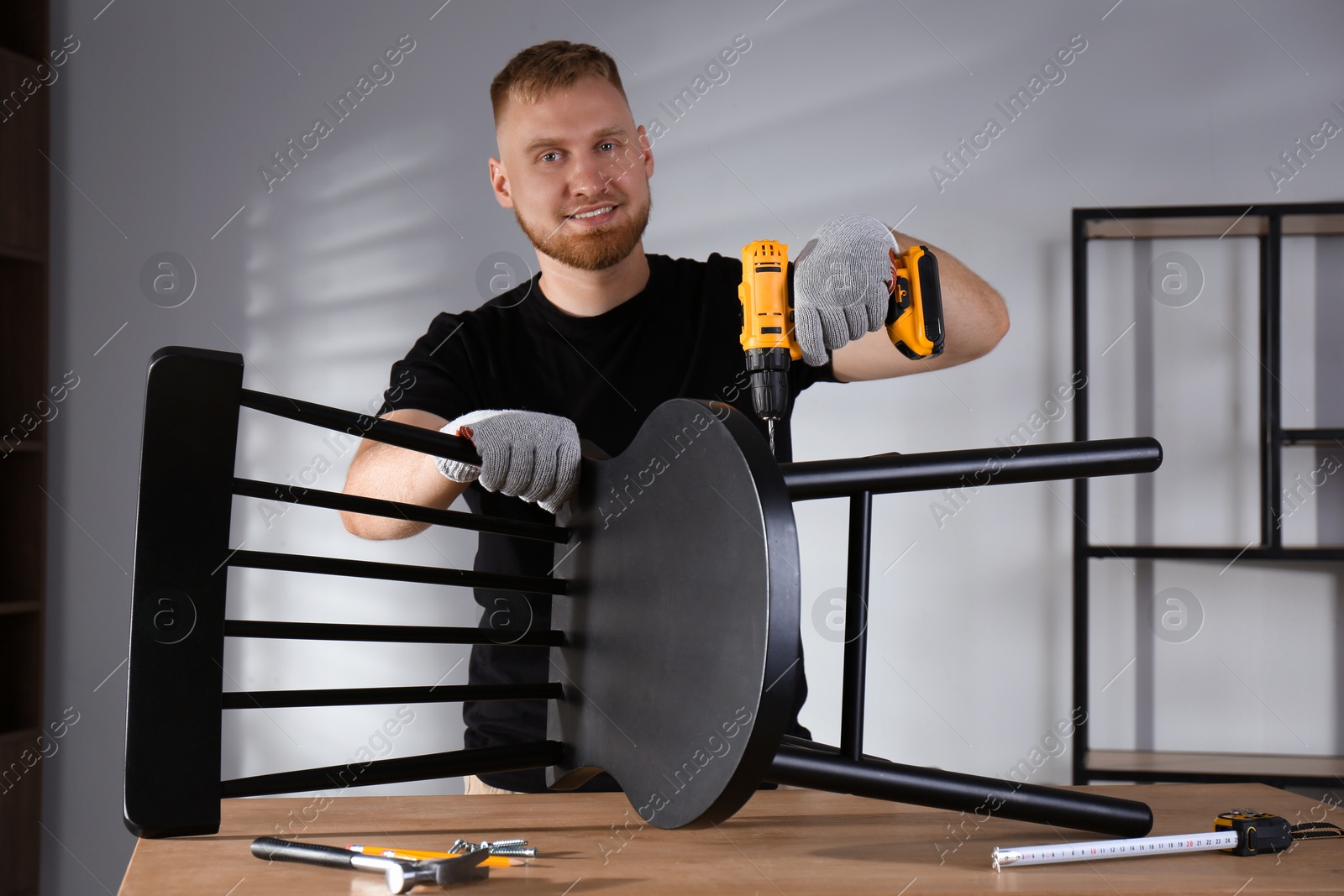 Photo of Man with electric screwdriver assembling chair in room