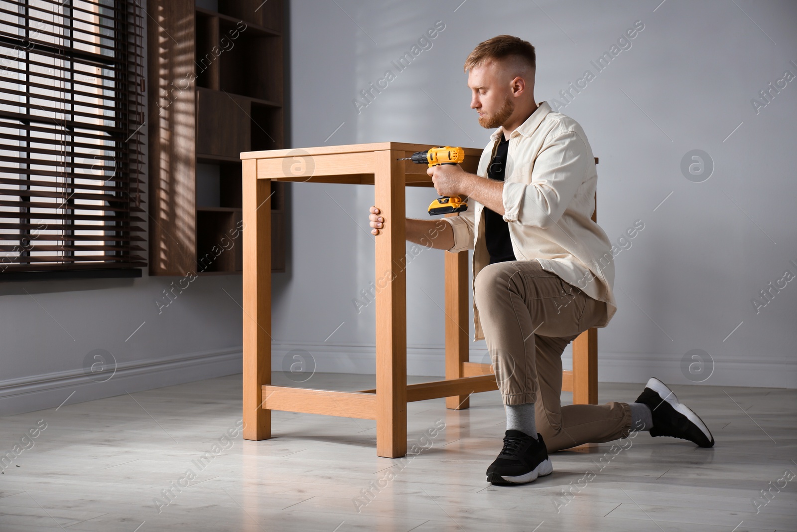 Photo of Man with electric screwdriver assembling table indoors