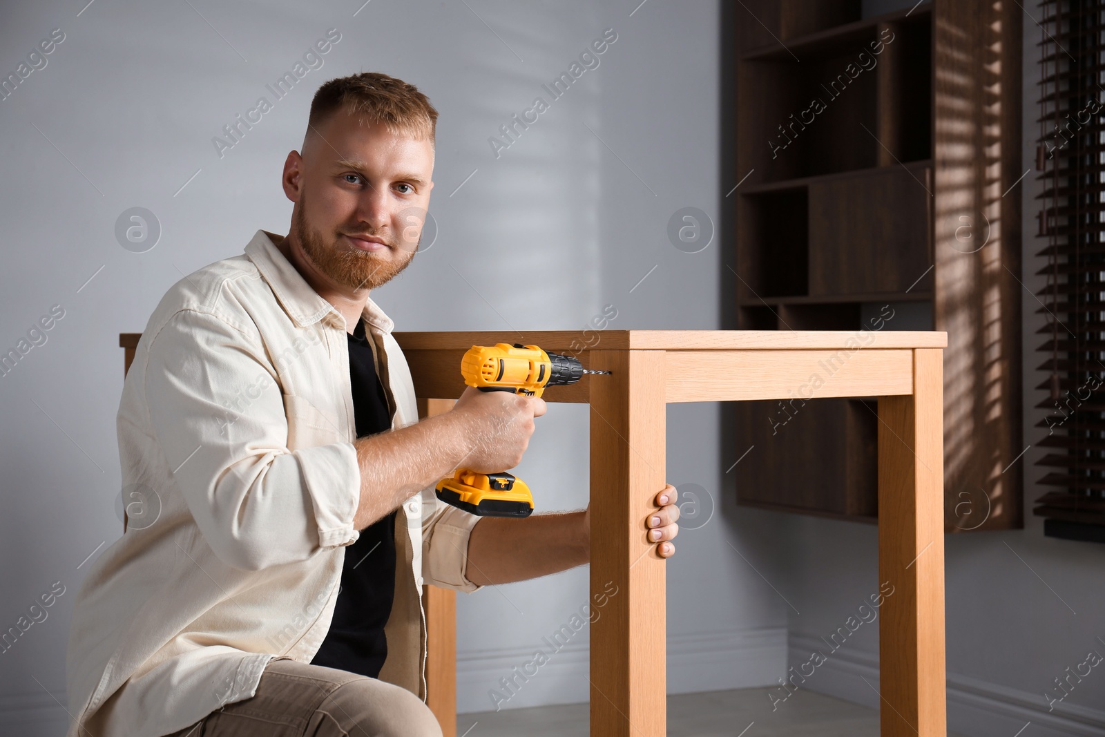 Photo of Man with electric screwdriver assembling table indoors