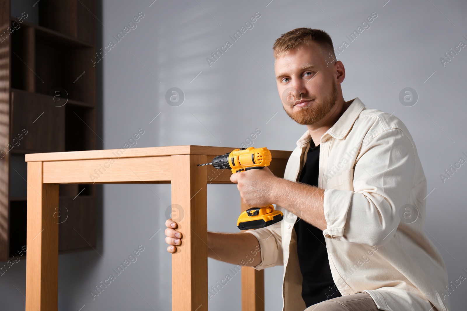 Photo of Man with electric screwdriver assembling table indoors