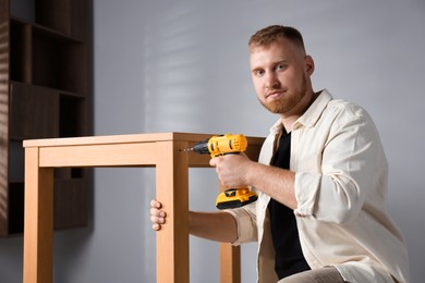 Photo of Man with electric screwdriver assembling table indoors