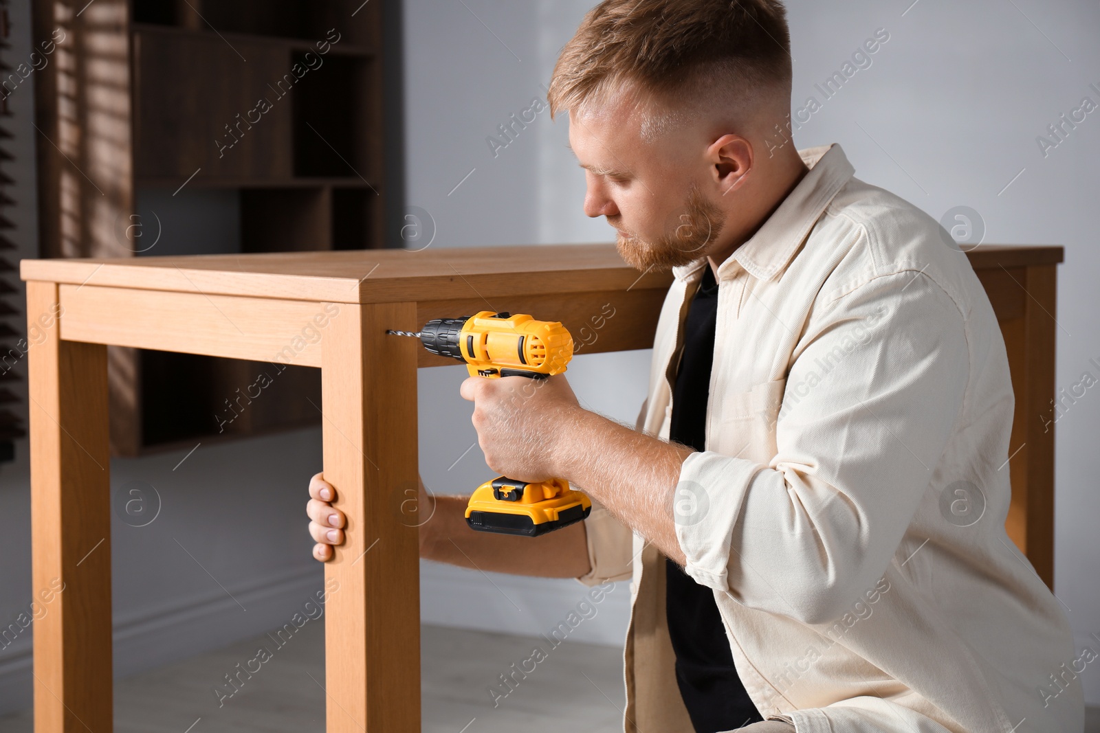 Photo of Man with electric screwdriver assembling table indoors