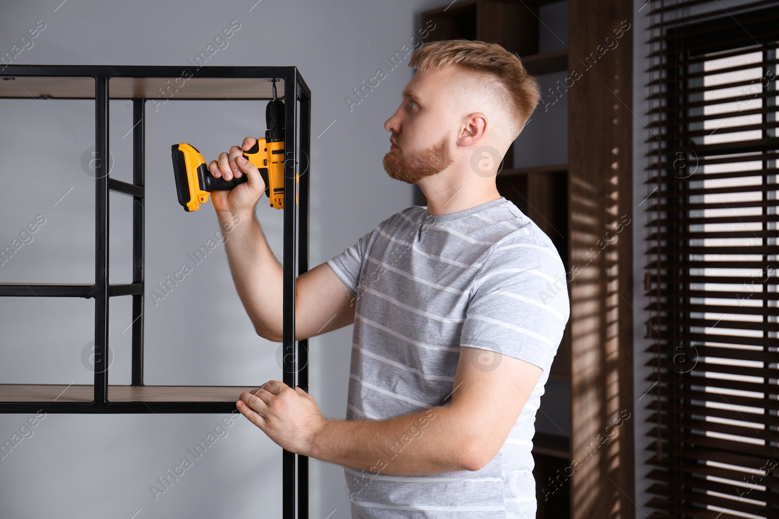 Photo of Man with electric screwdriver assembling shelving unit in room