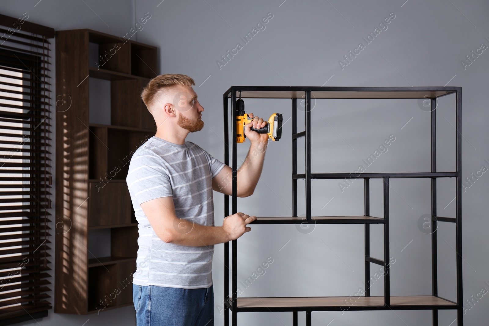 Photo of Man with electric screwdriver assembling shelving unit in room