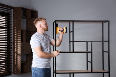 Photo of Man with electric screwdriver assembling shelving unit in room