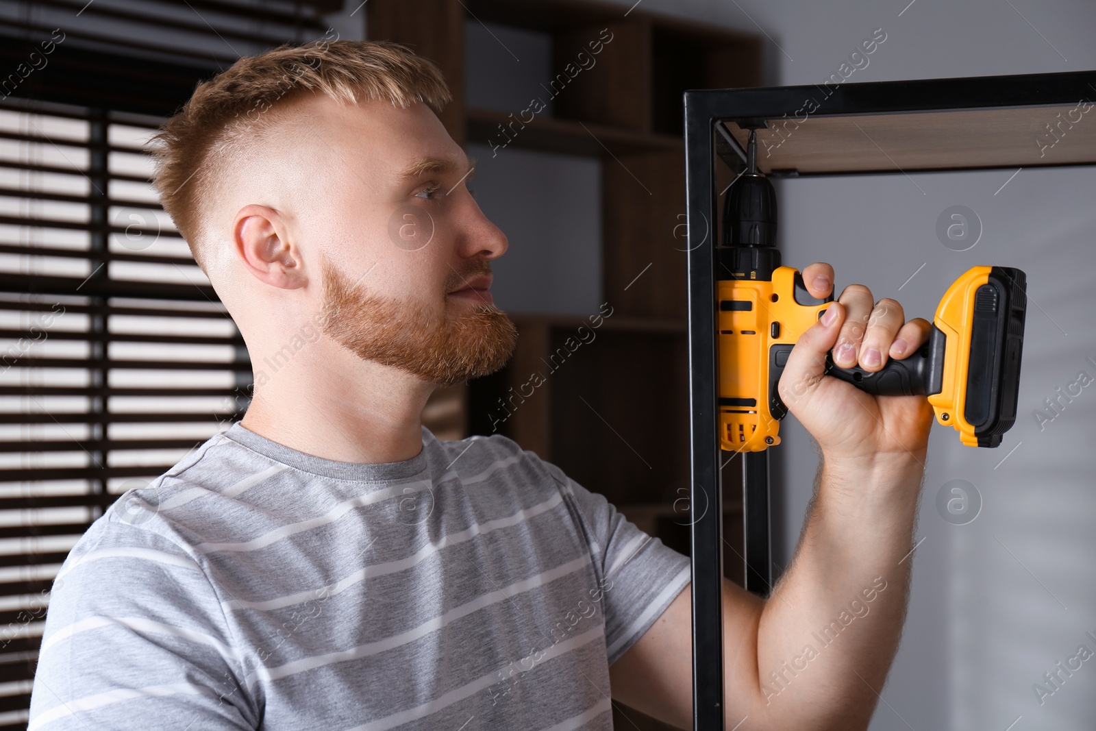 Photo of Man with electric screwdriver assembling shelving unit in room