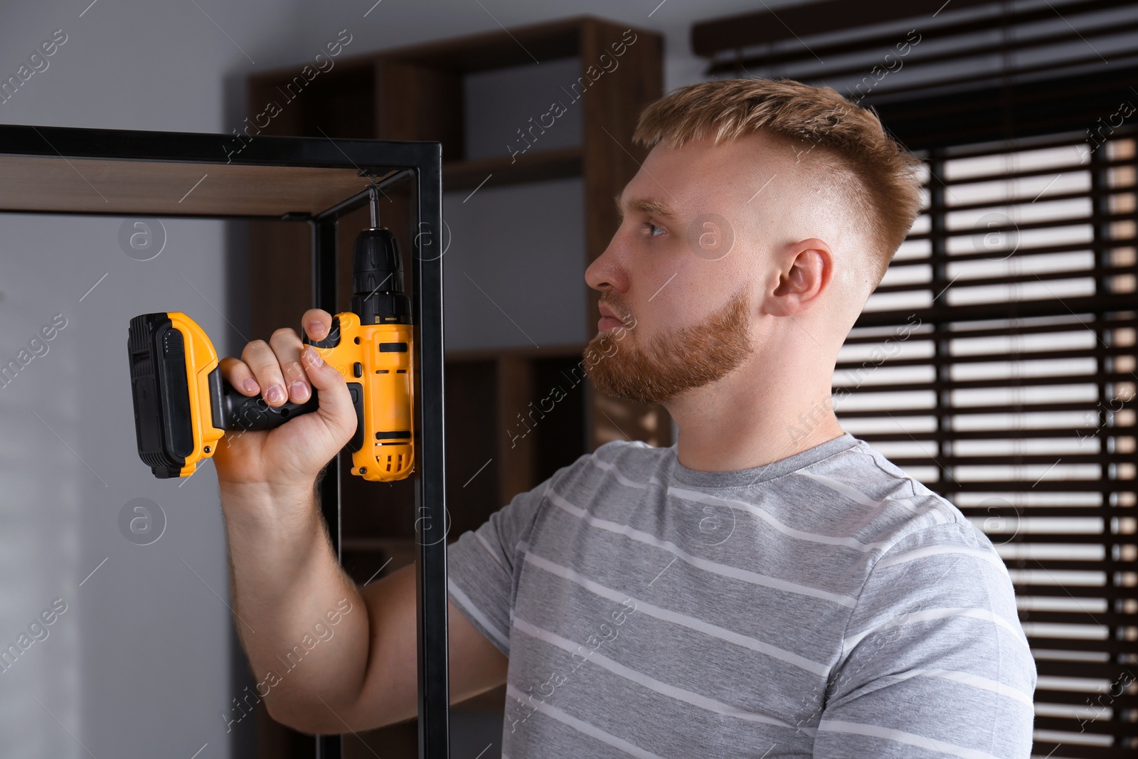 Photo of Man with electric screwdriver assembling shelving unit in room