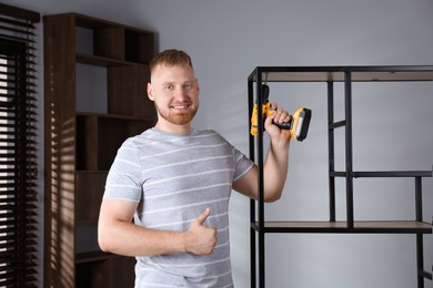 Photo of Man with electric screwdriver showing thumbs up at home. Assembling furniture