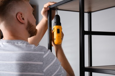 Photo of Man with electric screwdriver assembling furniture indoors