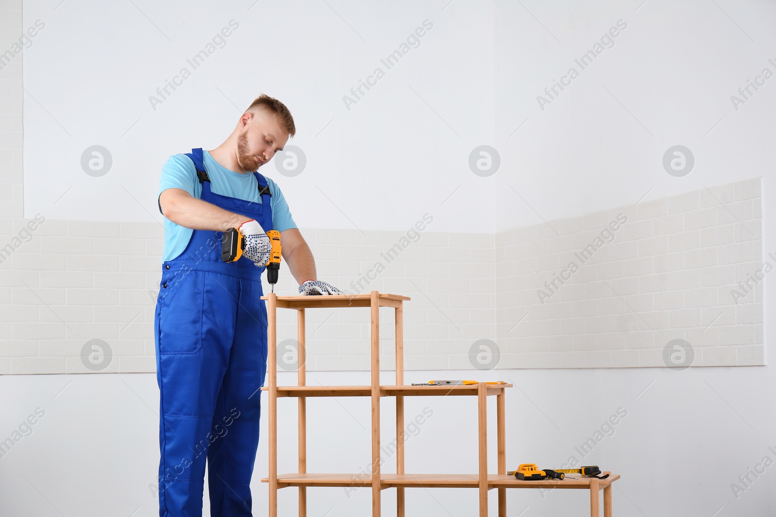 Photo of Worker with electric screwdriver assembling wooden shelving unit indoors