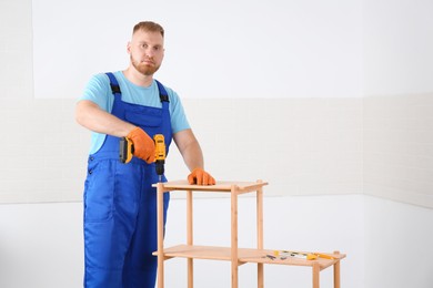 Photo of Worker with electric screwdriver assembling furniture indoors. Space for text