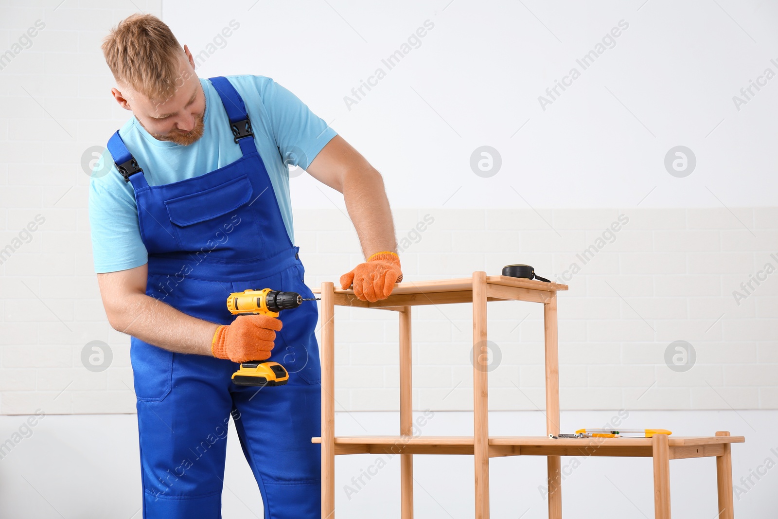 Photo of Worker with electric screwdriver assembling furniture indoors