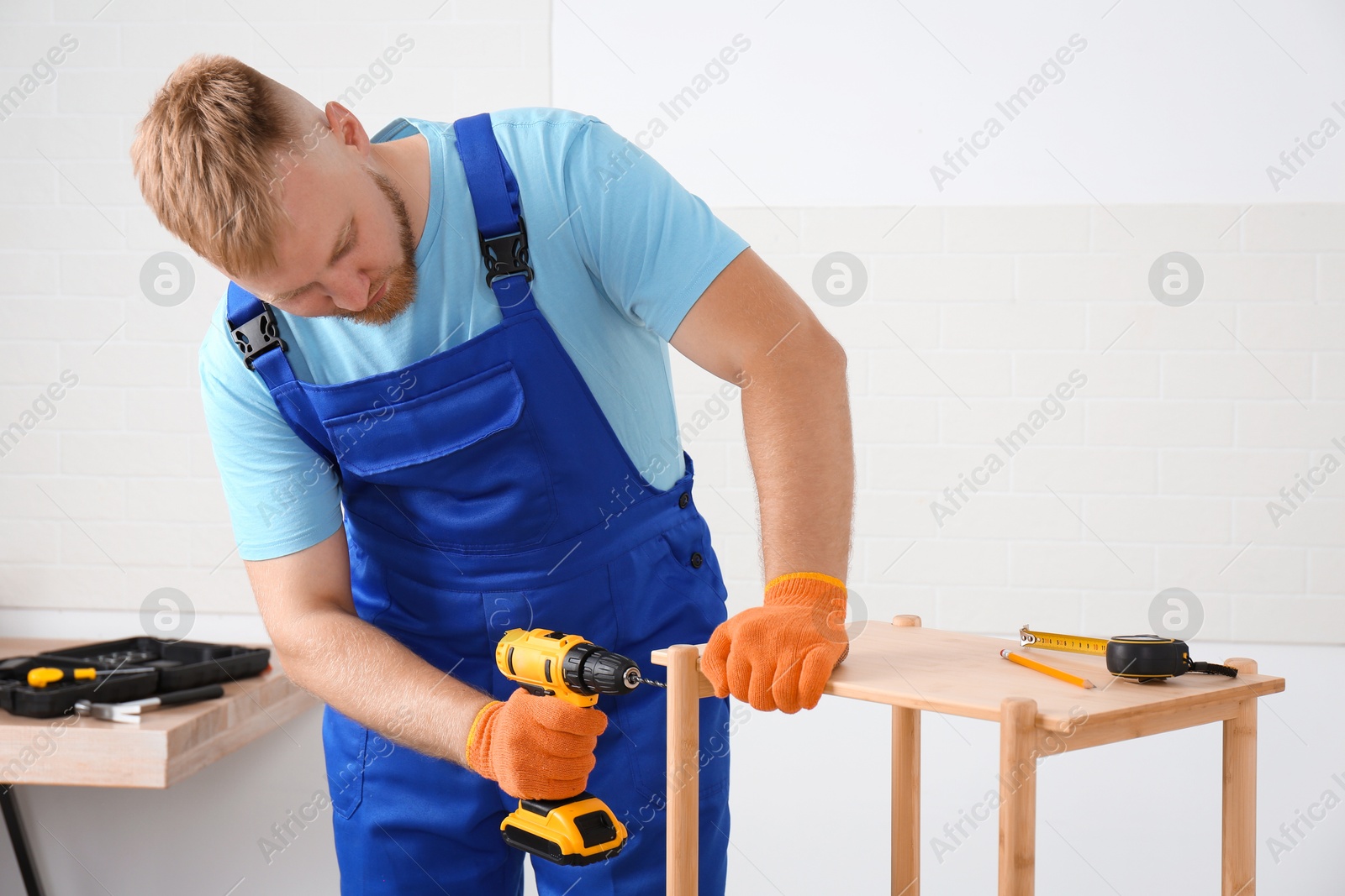 Photo of Worker with electric screwdriver assembling furniture indoors