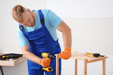 Worker with electric screwdriver assembling furniture indoors