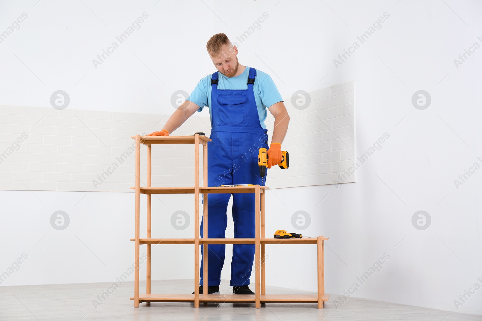 Photo of Worker with electric screwdriver assembling wooden shelving unit indoors