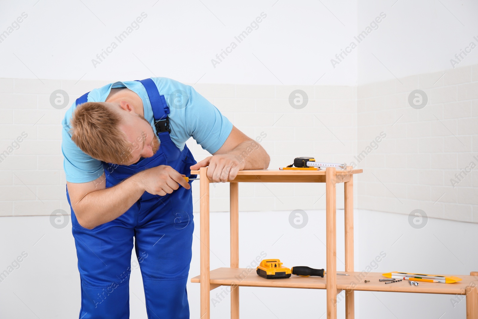 Photo of Worker with screwdriver assembling wooden furniture indoors