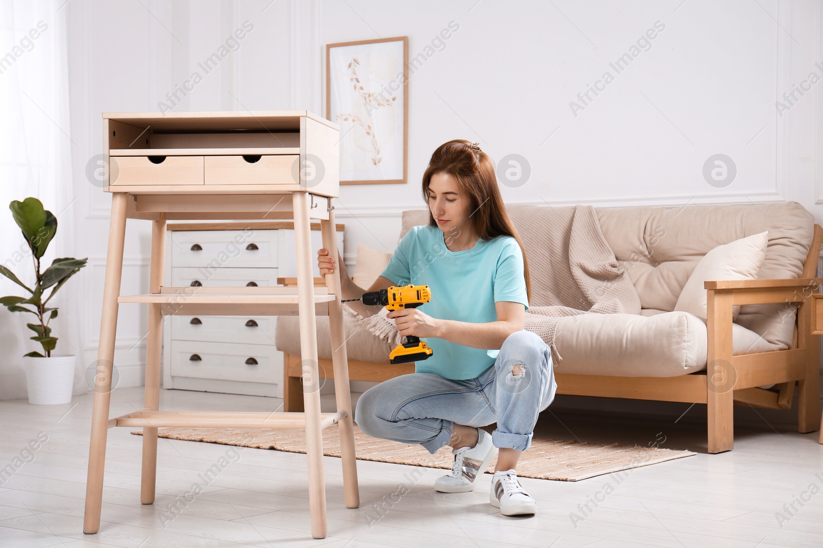 Photo of Woman with electric screwdriver assembling table in room