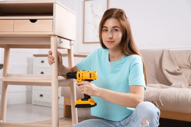 Woman with electric screwdriver assembling table in room