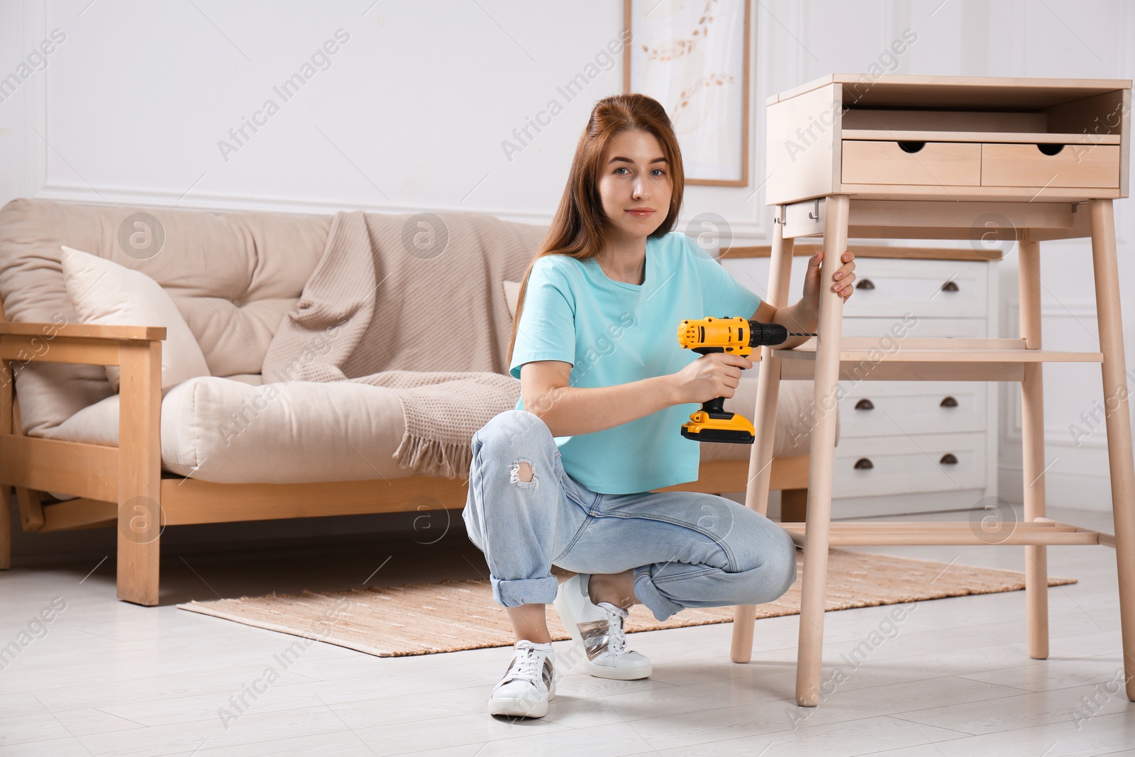 Photo of Woman with electric screwdriver assembling table in room