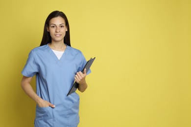 Portrait of smiling nurse with clipboard on yellow background. Space for text