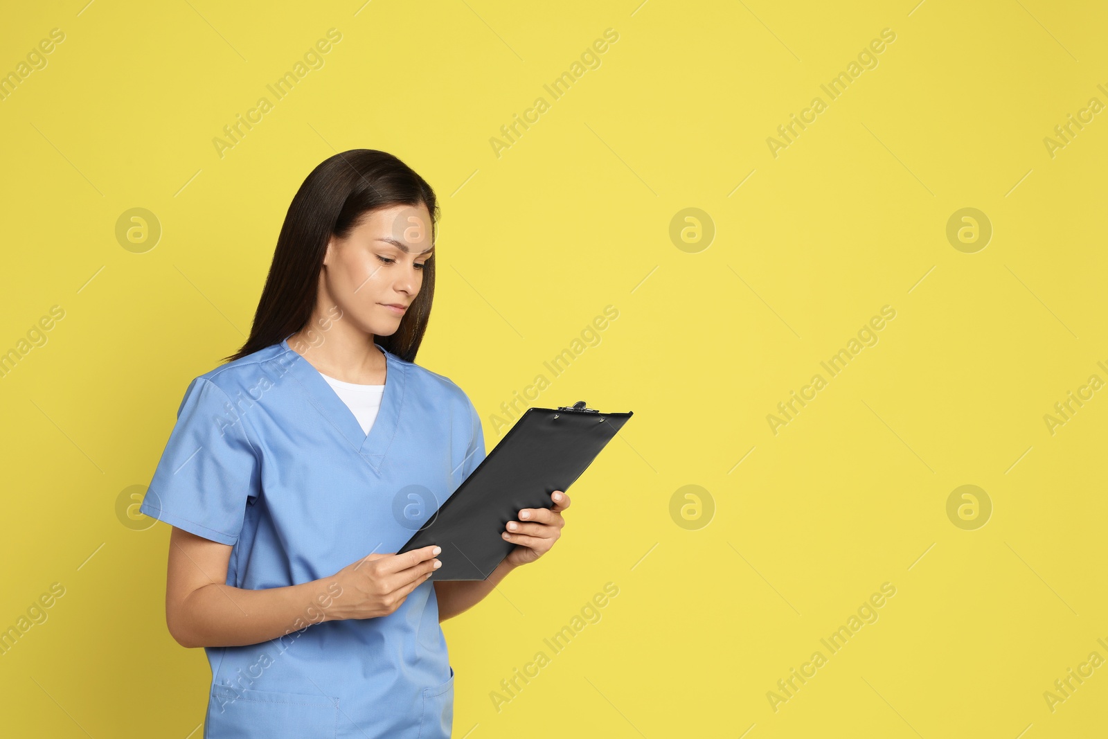 Photo of Portrait of beautiful nurse with clipboard on yellow background. Space for text