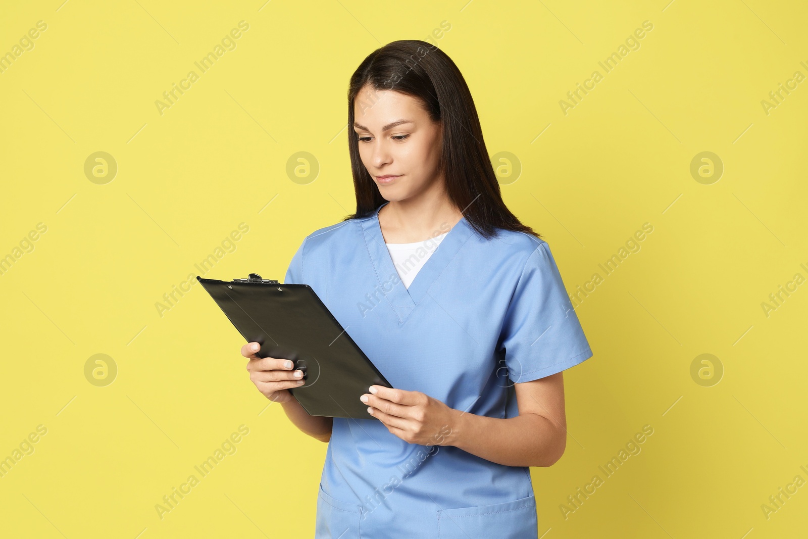 Photo of Portrait of beautiful nurse with clipboard on yellow background