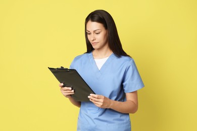 Portrait of beautiful nurse with clipboard on yellow background