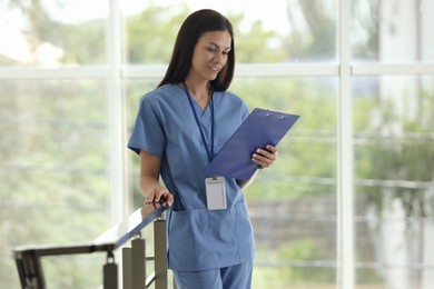 Photo of Smiling nurse with clipboard near railings in hospital