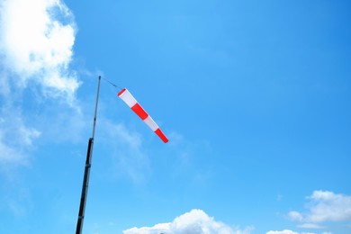 Striped windsock on pole against blue sky, space for text