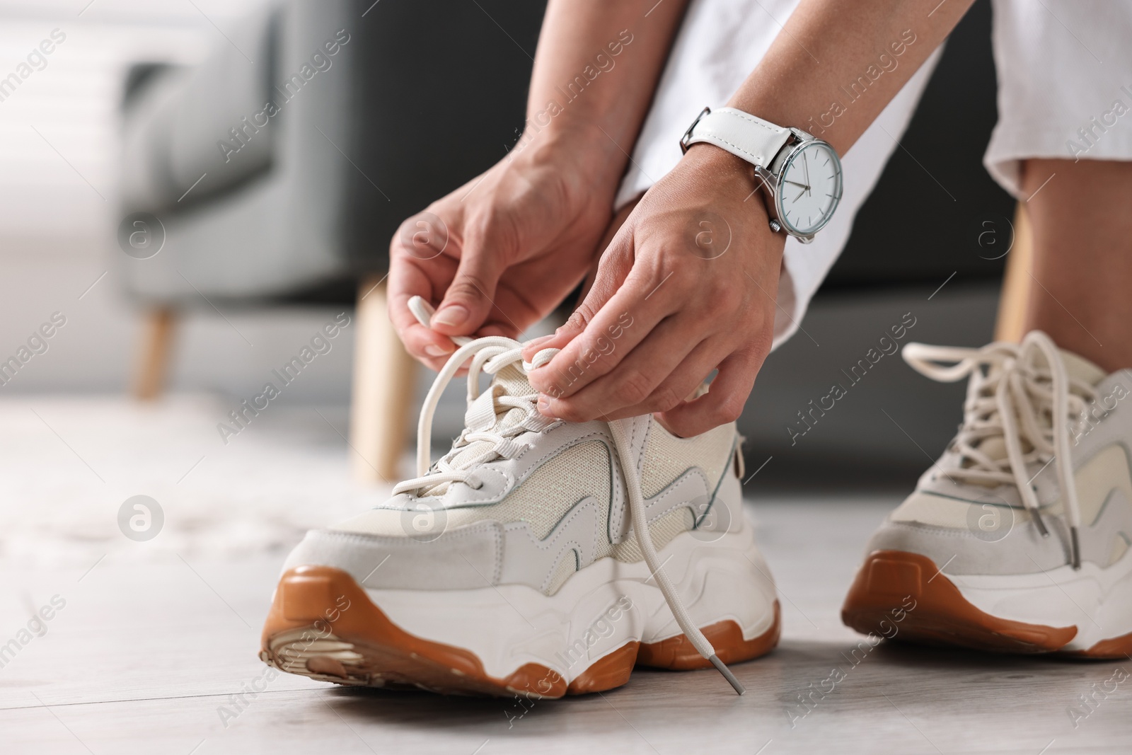 Photo of Woman tying shoelace of sneaker indoors, closeup