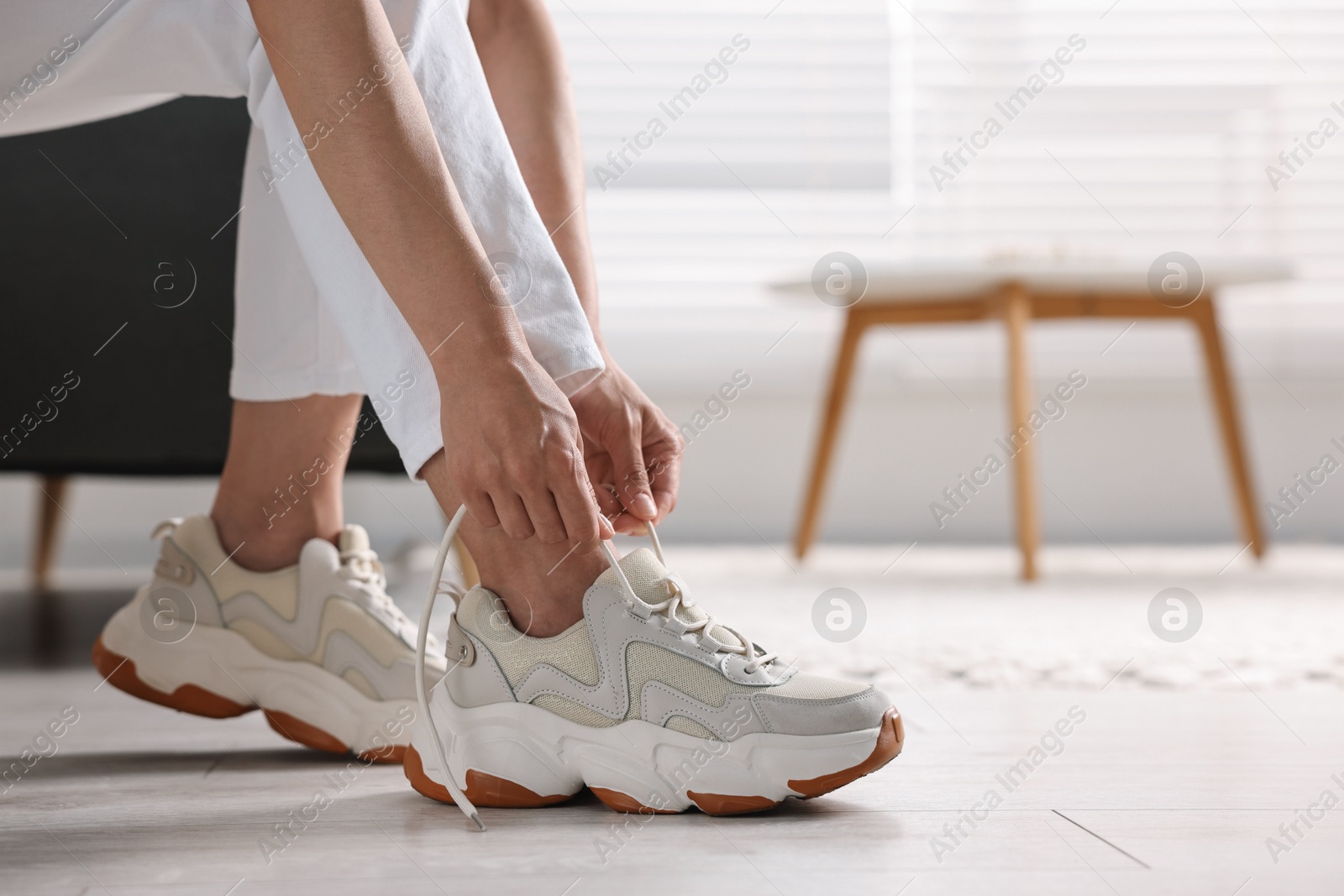 Photo of Woman tying shoelace of sneaker indoors, closeup. Space for text