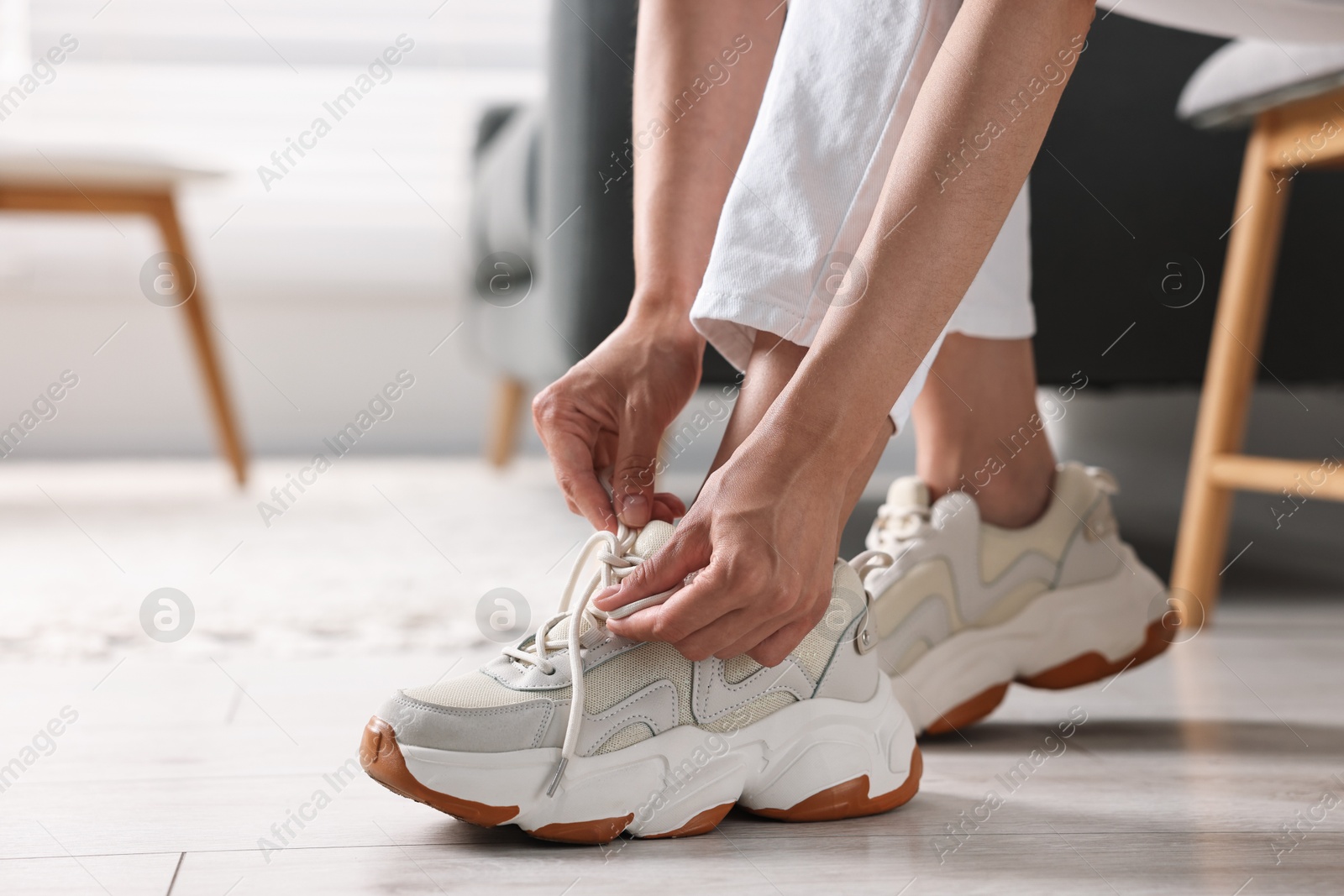 Photo of Woman tying shoelace of sneaker indoors, closeup. Space for text