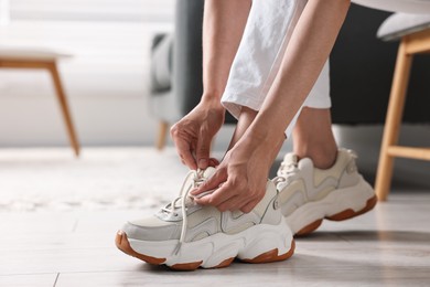 Photo of Woman tying shoelace of sneaker indoors, closeup. Space for text