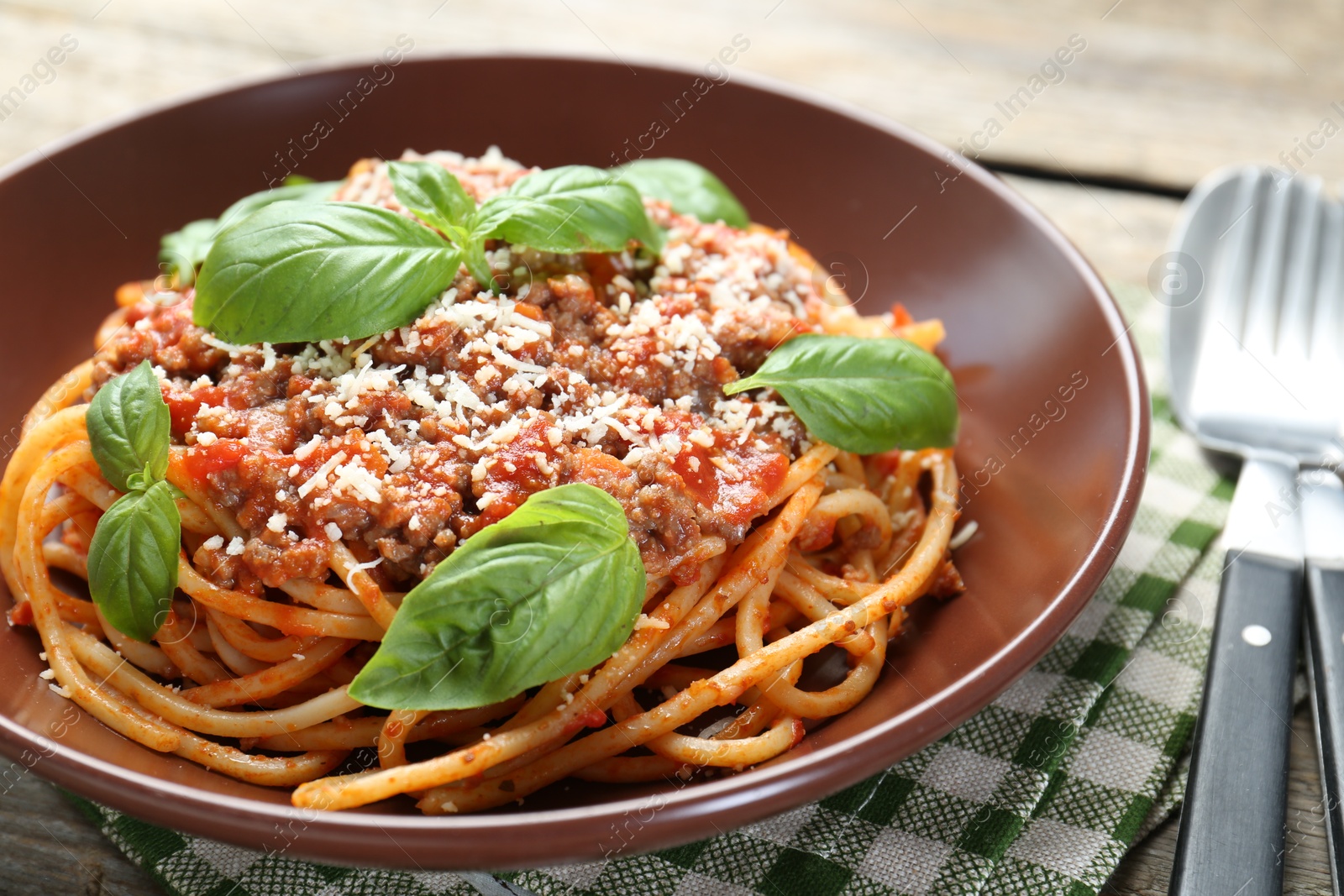 Photo of Delicious pasta bolognese with basil and cutlery on table, closeup