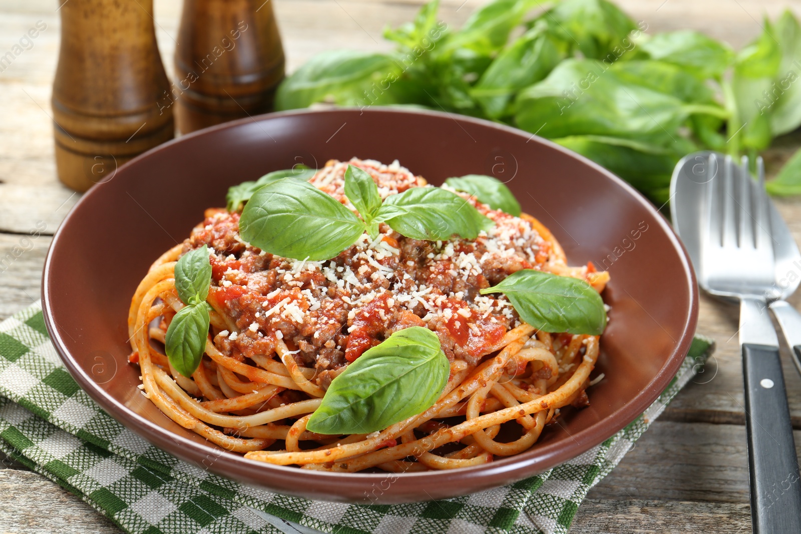 Photo of Delicious pasta bolognese with basil and cutlery on wooden table, closeup