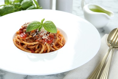 Photo of Delicious pasta bolognese with basil and cutlery on white marble table, closeup