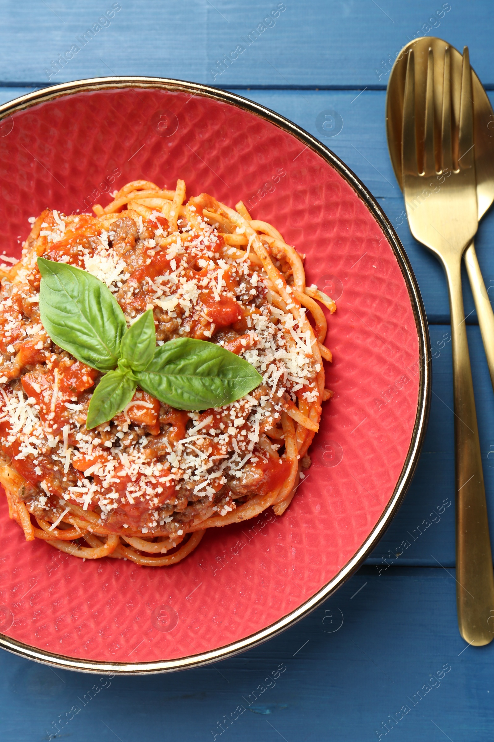 Photo of Delicious pasta bolognese with basil and cutlery on blue wooden table, top view