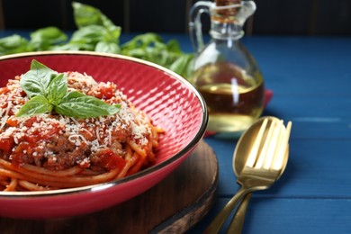 Photo of Delicious pasta bolognese with basil and cutlery on blue wooden table, closeup