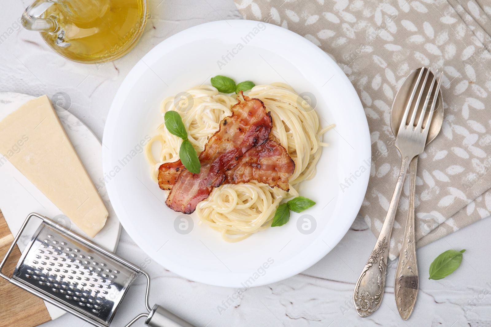 Photo of Delicious pasta Carbonara, cheese, oil, cutlery and grater on light textured table, flat lay