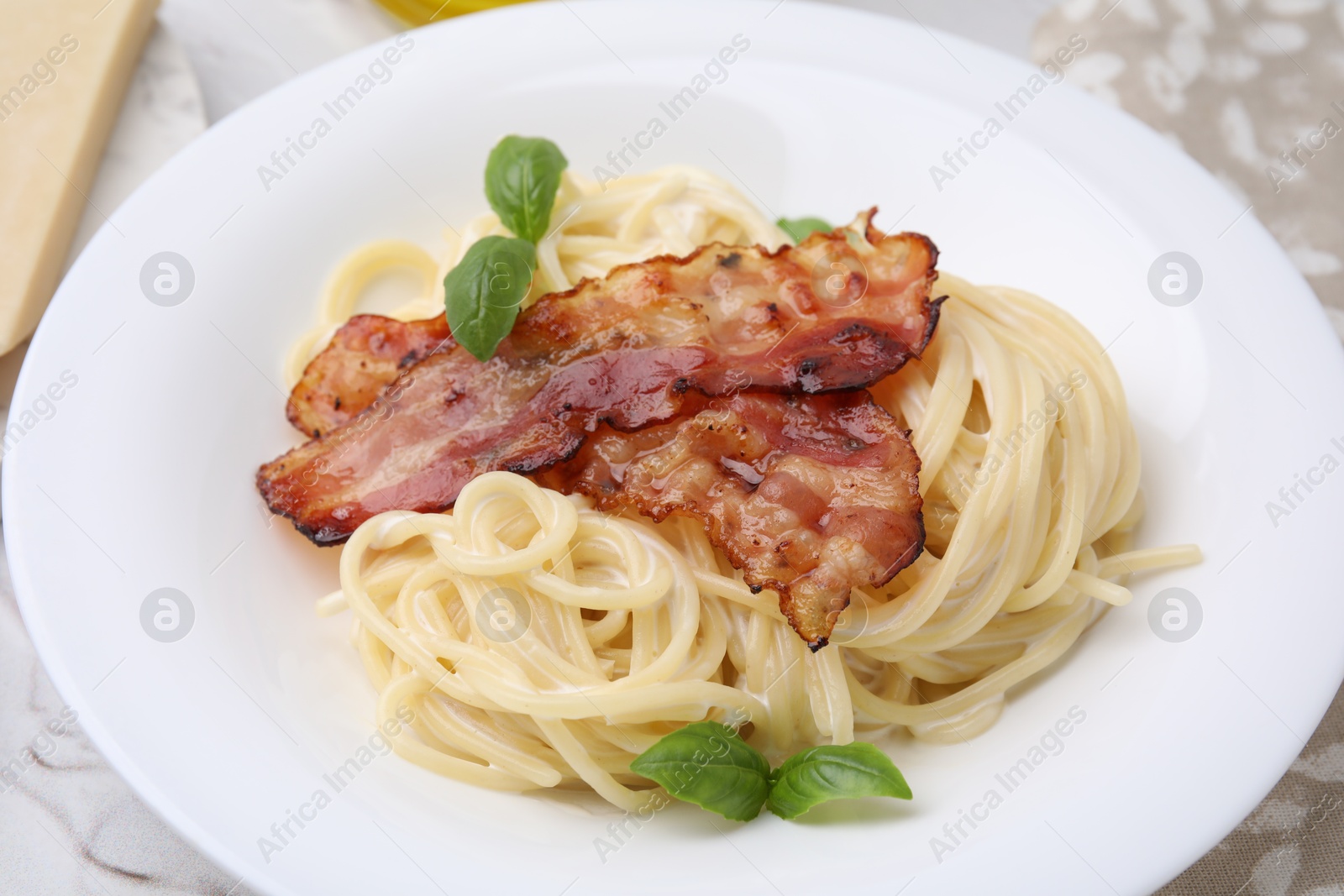 Photo of Delicious pasta Carbonara with bacon and basil on table, closeup