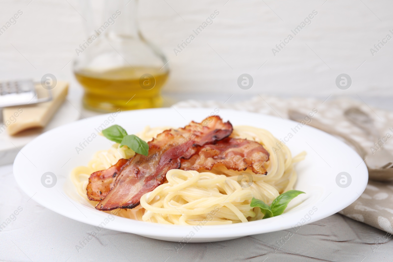 Photo of Delicious pasta Carbonara with bacon and basil on light table, closeup