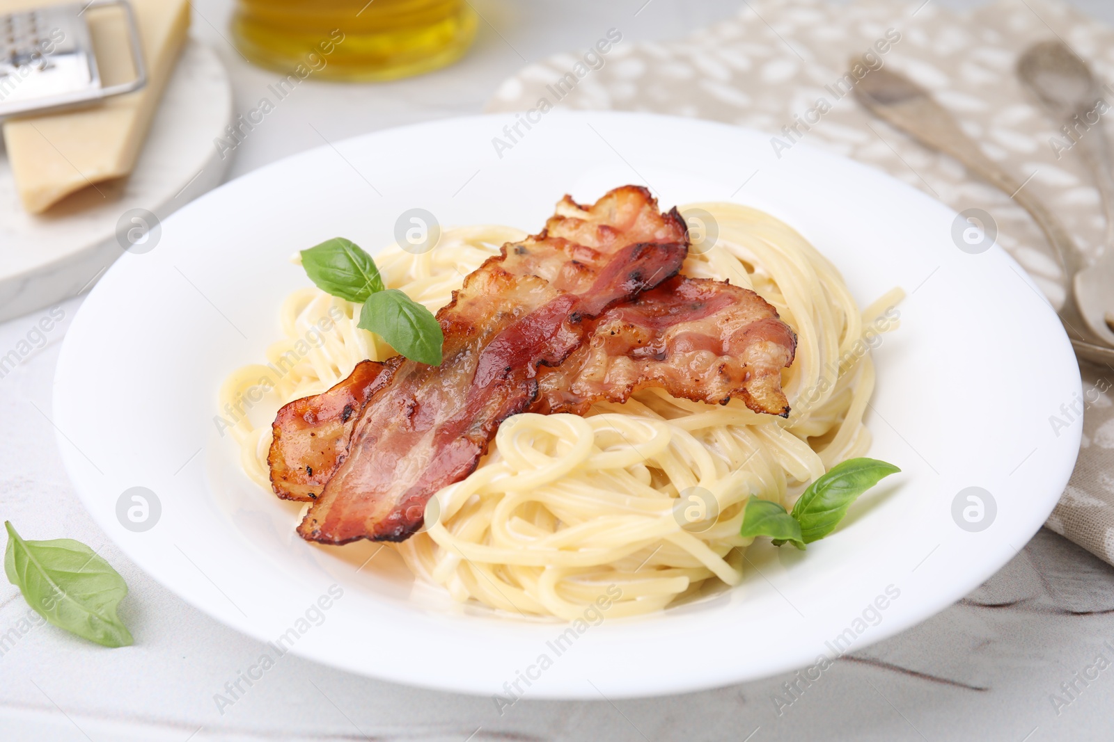 Photo of Delicious pasta Carbonara with bacon and basil on light table, closeup