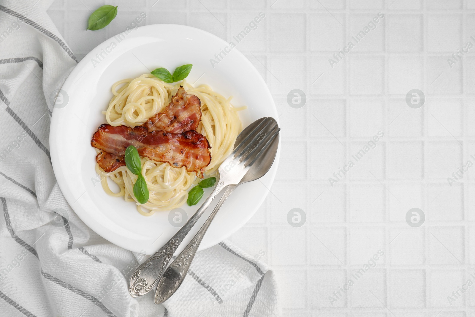 Photo of Delicious pasta Carbonara served on white tiled table, top view. Space for text