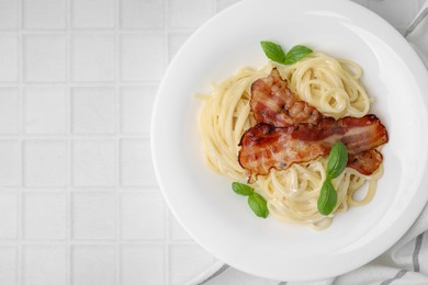 Delicious pasta Carbonara with bacon and basil on white tiled table, top view. Space for text