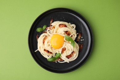 Photo of Delicious pasta Carbonara with egg yolk, bacon and basil on green table, top view