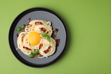 Photo of Delicious pasta Carbonara with egg yolk, bacon and basil on green table, top view. Space for text