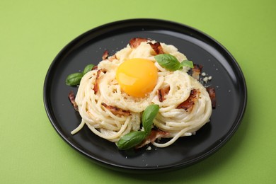 Photo of Delicious pasta Carbonara with egg yolk, bacon and basil on green table, closeup