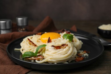 Photo of Delicious pasta Carbonara with egg yolk, bacon and basil on wooden table, closeup