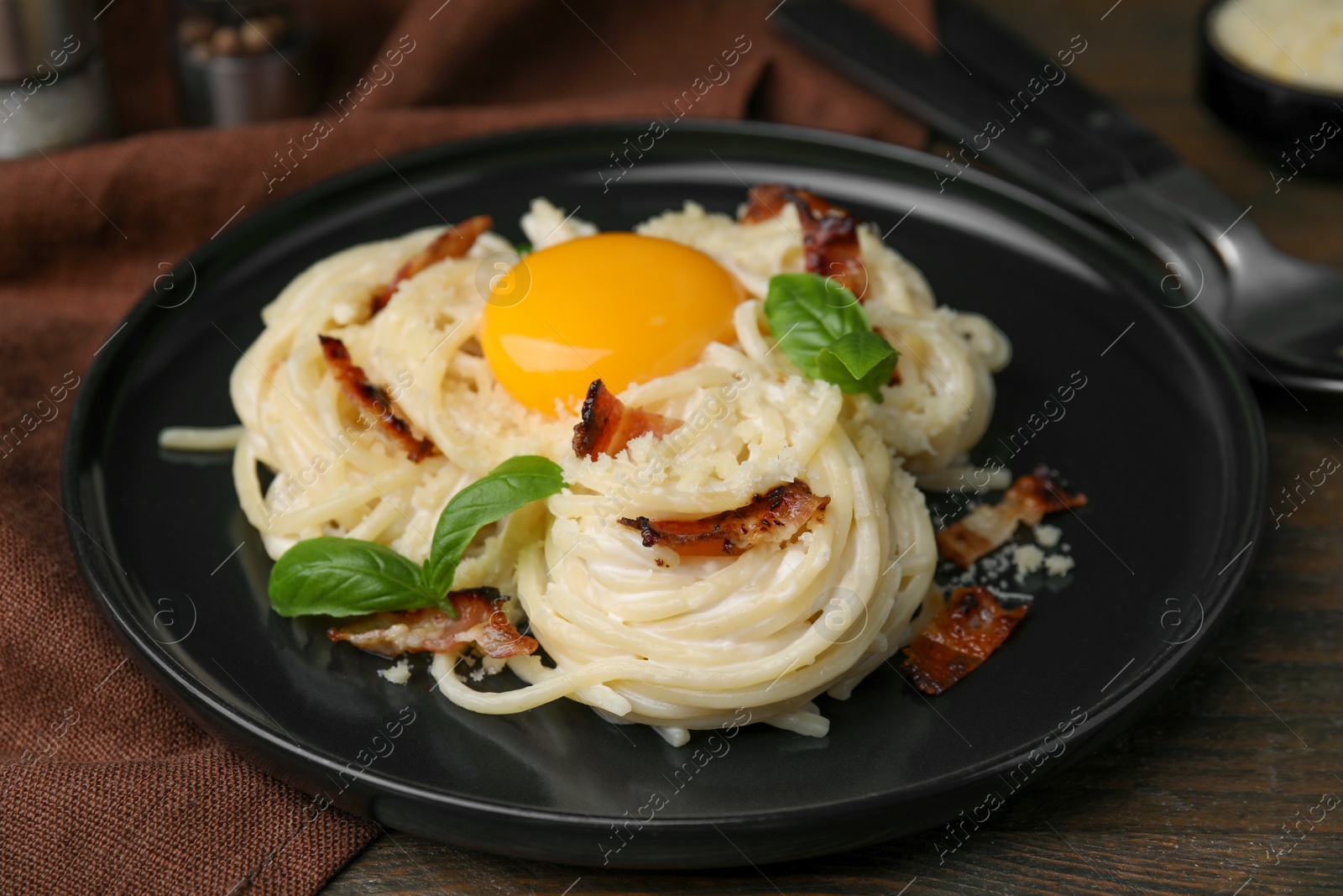 Photo of Delicious pasta Carbonara with egg yolk, bacon and basil on wooden table, closeup