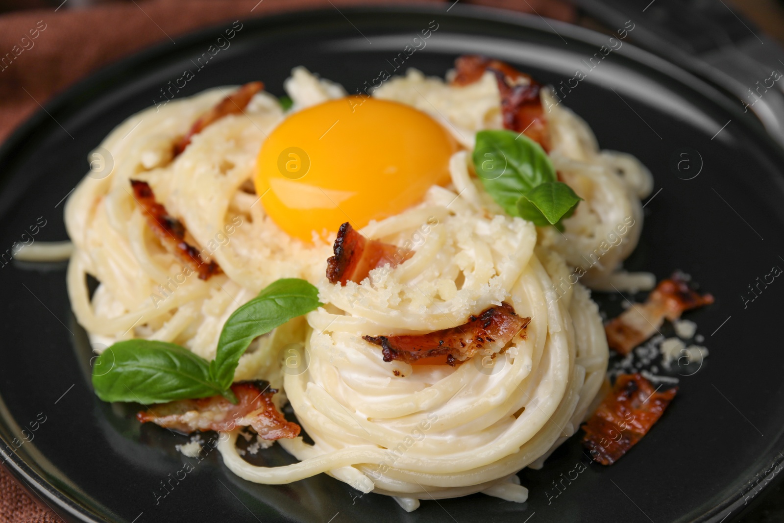 Photo of Delicious pasta Carbonara with egg yolk, bacon and basil on plate, closeup